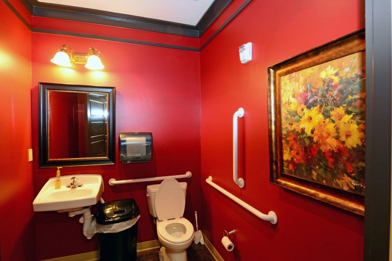 A stylish bathroom with red walls, featuring a toilet, sink, mirror, and artwork.