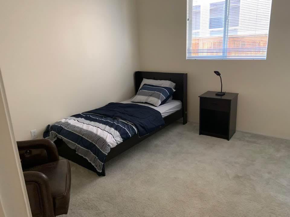 A minimalist bedroom with a single bed, nightstand, and lamp.