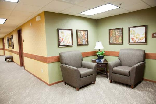 A cozy waiting area featuring two comfortable chairs, a small table with a lamp, and framed artwork on the walls.