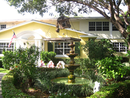 A charming yellow house surrounded by lush greenery and a serene fountain in the garden.
