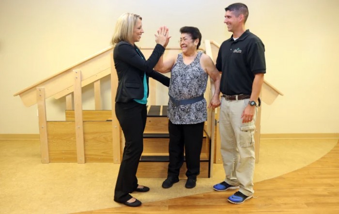 A physical therapy session with a patient supported by two therapists.