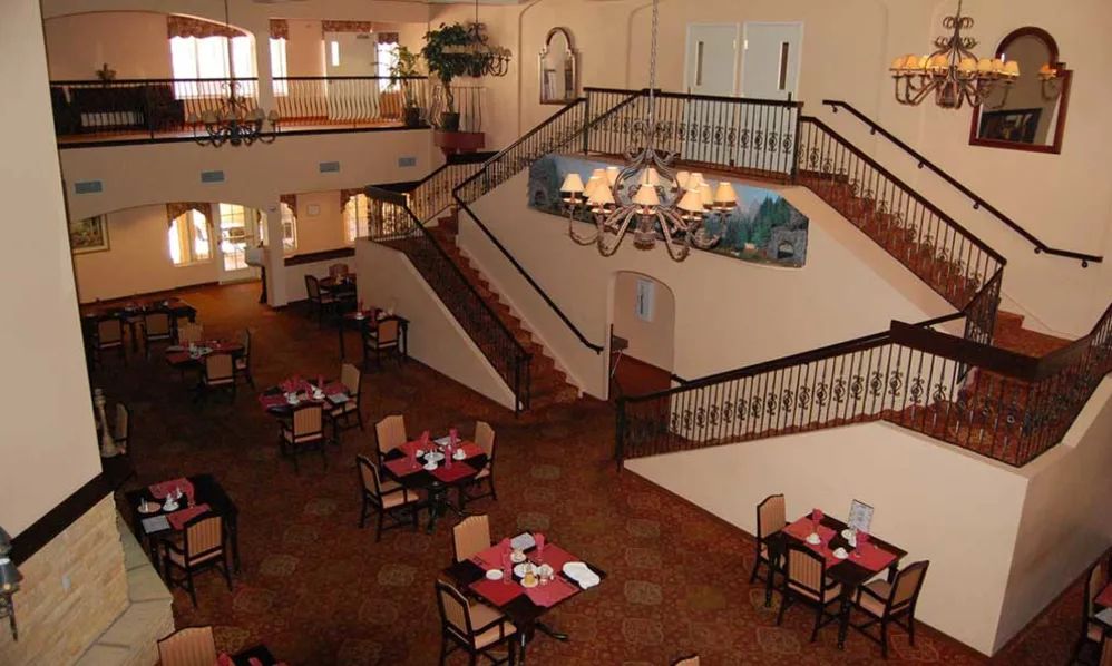 A spacious restaurant interior featuring a central staircase and elegantly set tables.