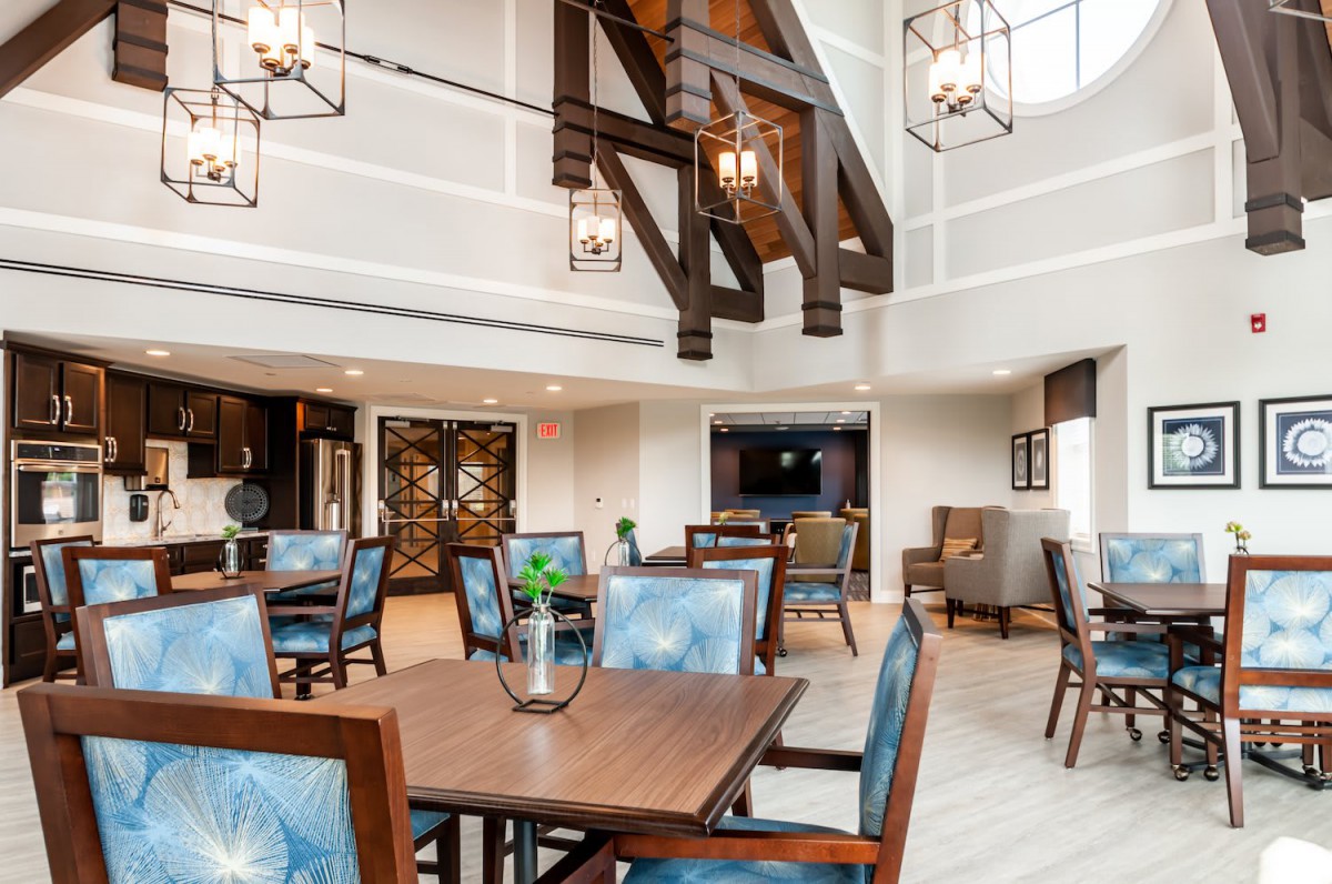 A modern dining area with high ceilings and wooden beams, featuring elegant chandeliers and comfortable seating.