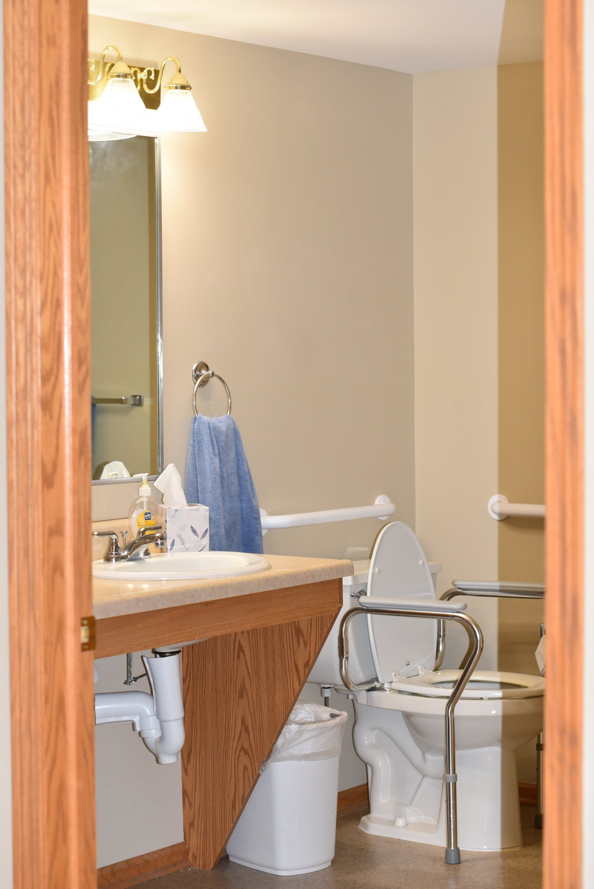 A bathroom with an accessible toilet, grab bars, and a sink reflected in the mirror.