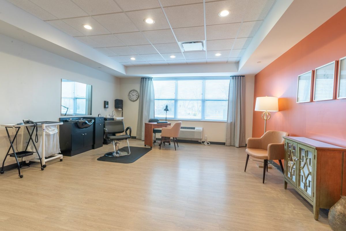 A spacious salon room with a large window, chairs, and a mirror.