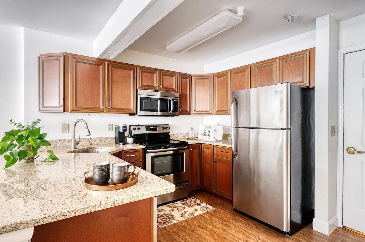 A modern kitchen with wood cabinets and granite countertops, featuring stainless steel appliances.