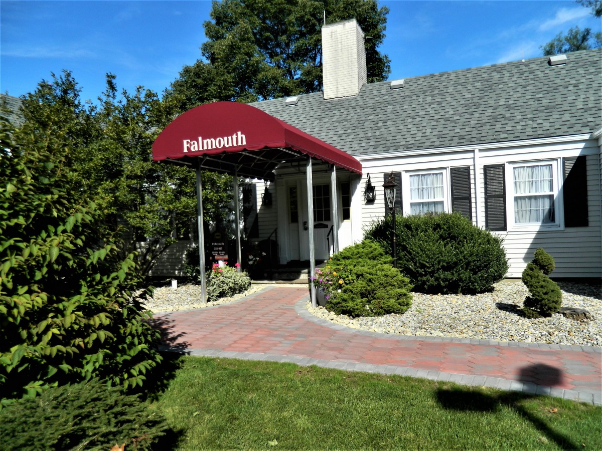 A quaint house with a red canopy entrance surrounded by greenery and a brick pathway.