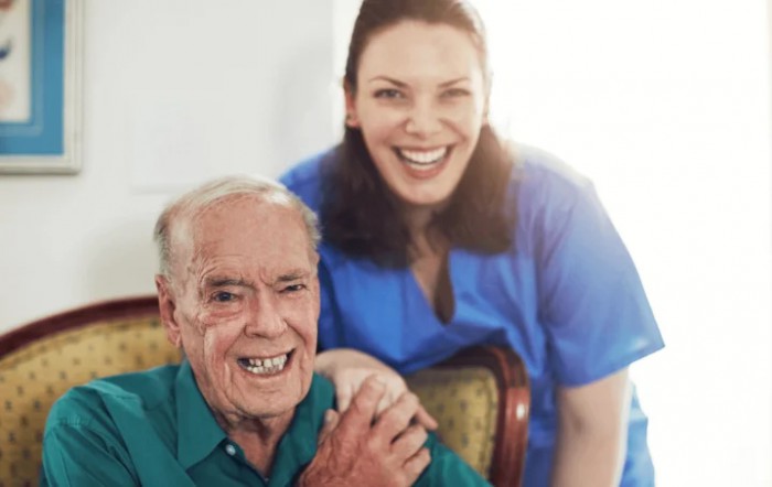 An elderly man sitting with a caregiver, both smiling.