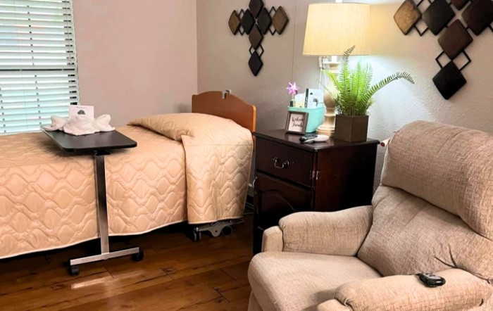 A cozy bedroom with a hospital bed, armchair, and side table with a lamp.