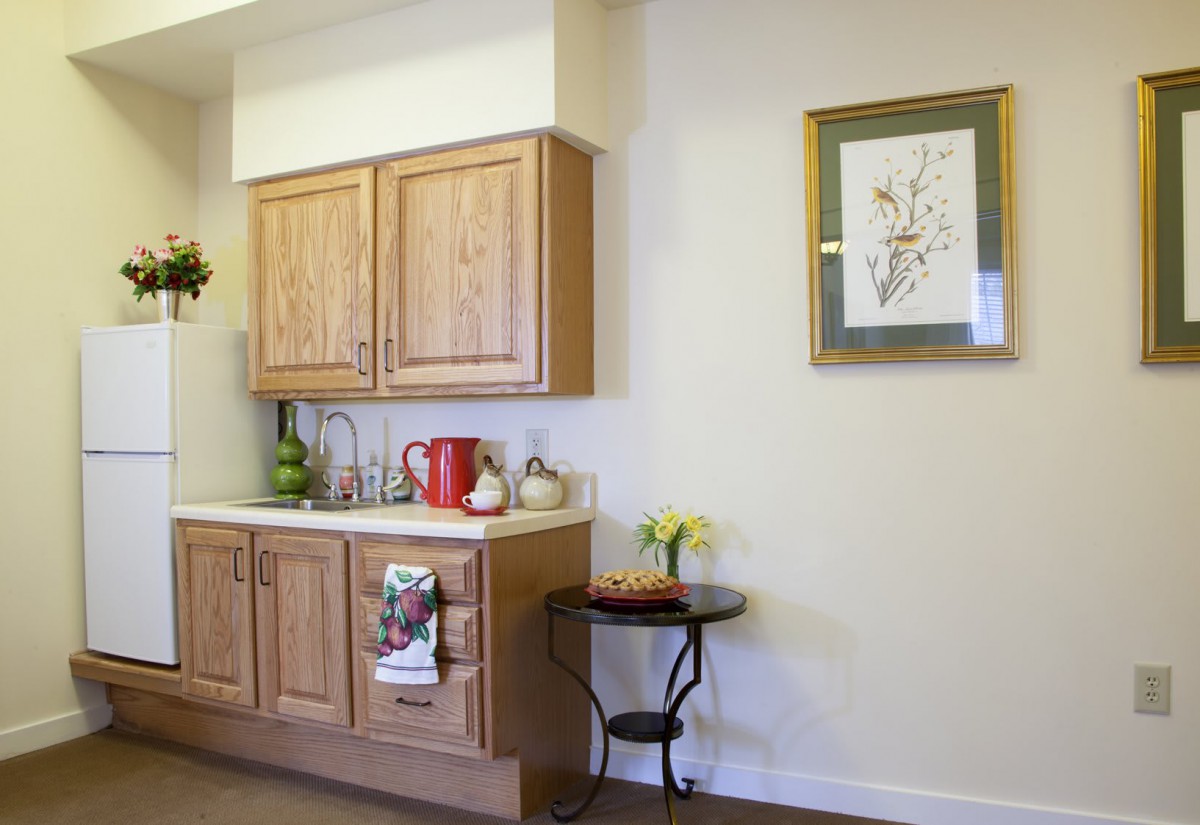 A cozy kitchen nook with wooden cabinets, a countertop with a red kettle, and decorative artwork on the wall.