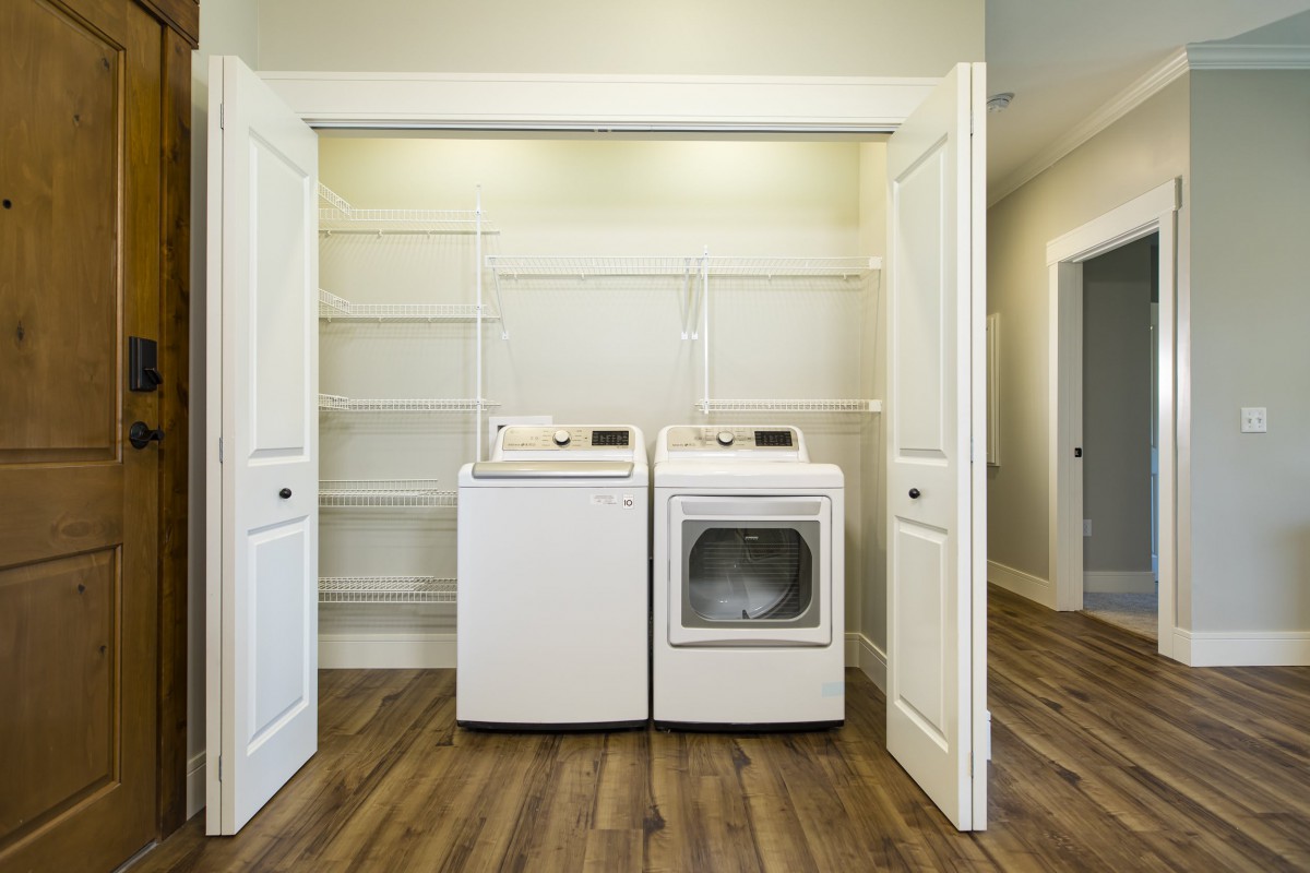 A laundry room with a washing machine, dryer, and shelves on a wooden floor.