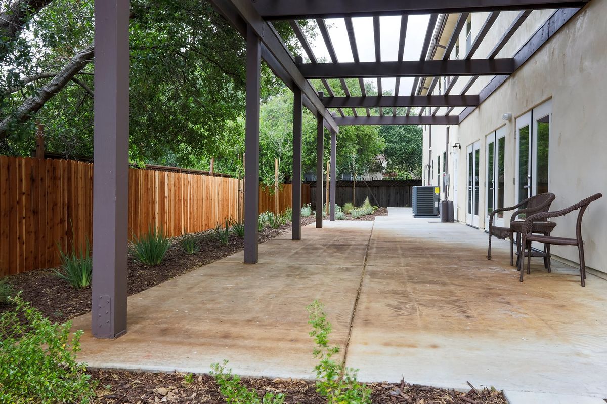 A modern backyard patio with a pergola and surrounding greenery.