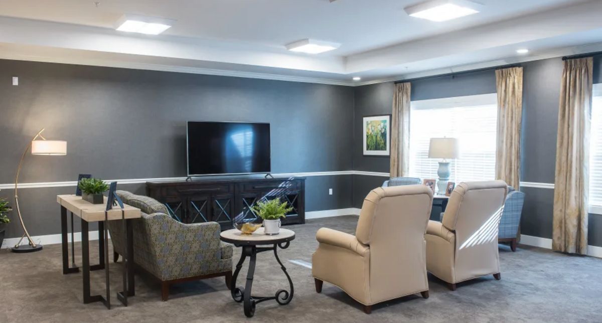A cozy living room featuring comfortable armchairs facing a large television, with a small table in the center.