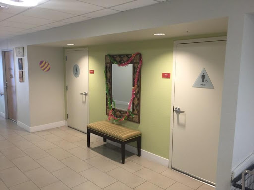 A hallway featuring restroom signs, a mirror, and a bench.