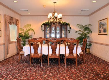 A traditional dining room with a large table, surrounded by chairs, and lit by a chandelier.