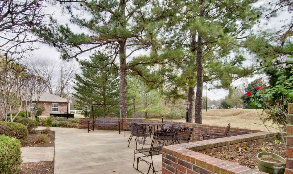 A peaceful outdoor patio area with tables and chairs surrounded by trees and brick walls.