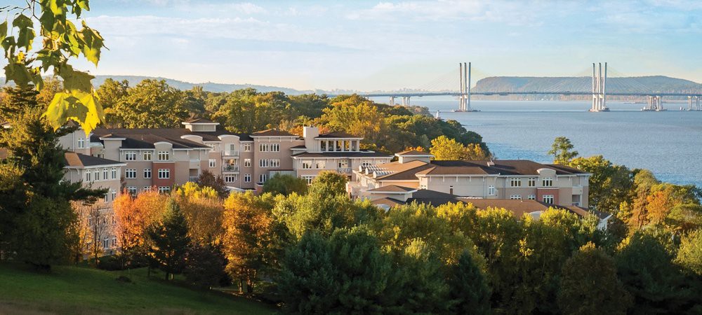 Scenic view of buildings surrounded by lush greenery and a bridge over a river.