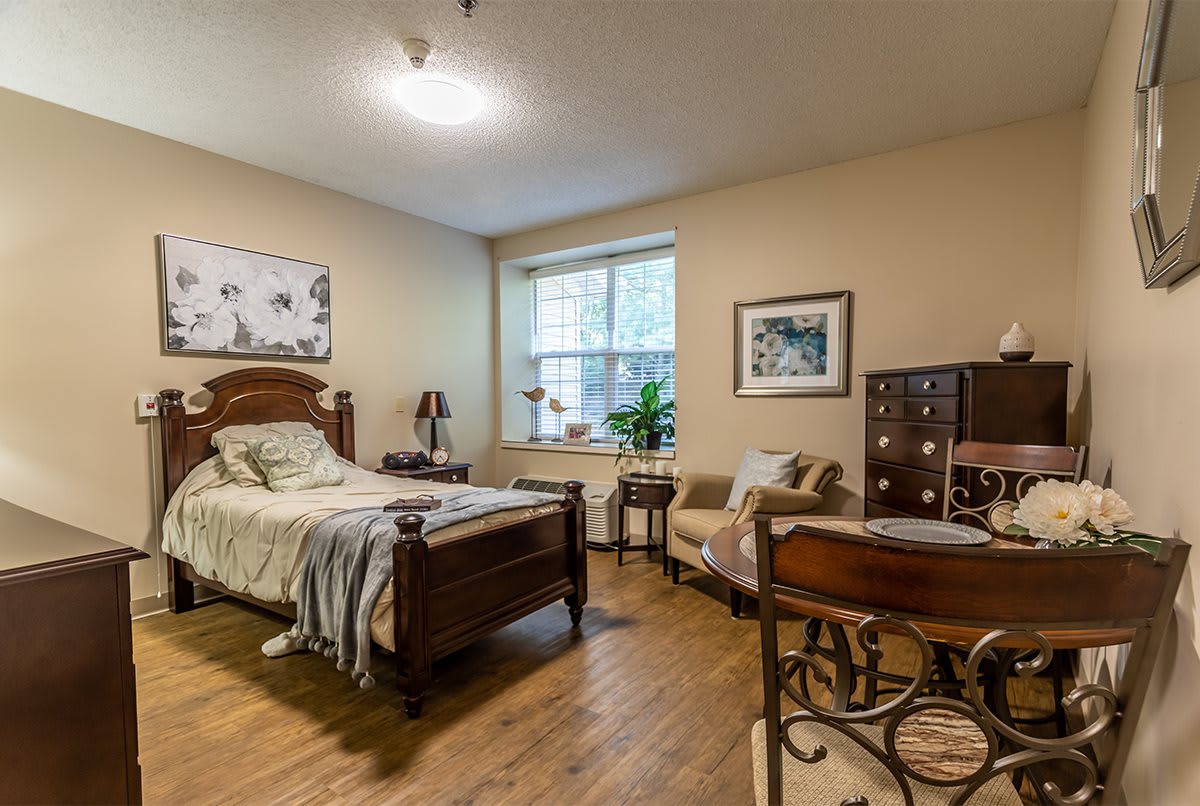 A cozy bedroom with a wooden bed, armchair, and large window.