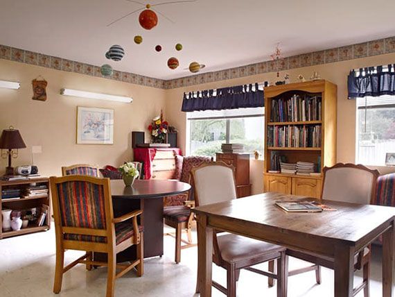 A cozy dining room with a table, chairs, bookshelf, and a model solar system hanging from the ceiling.