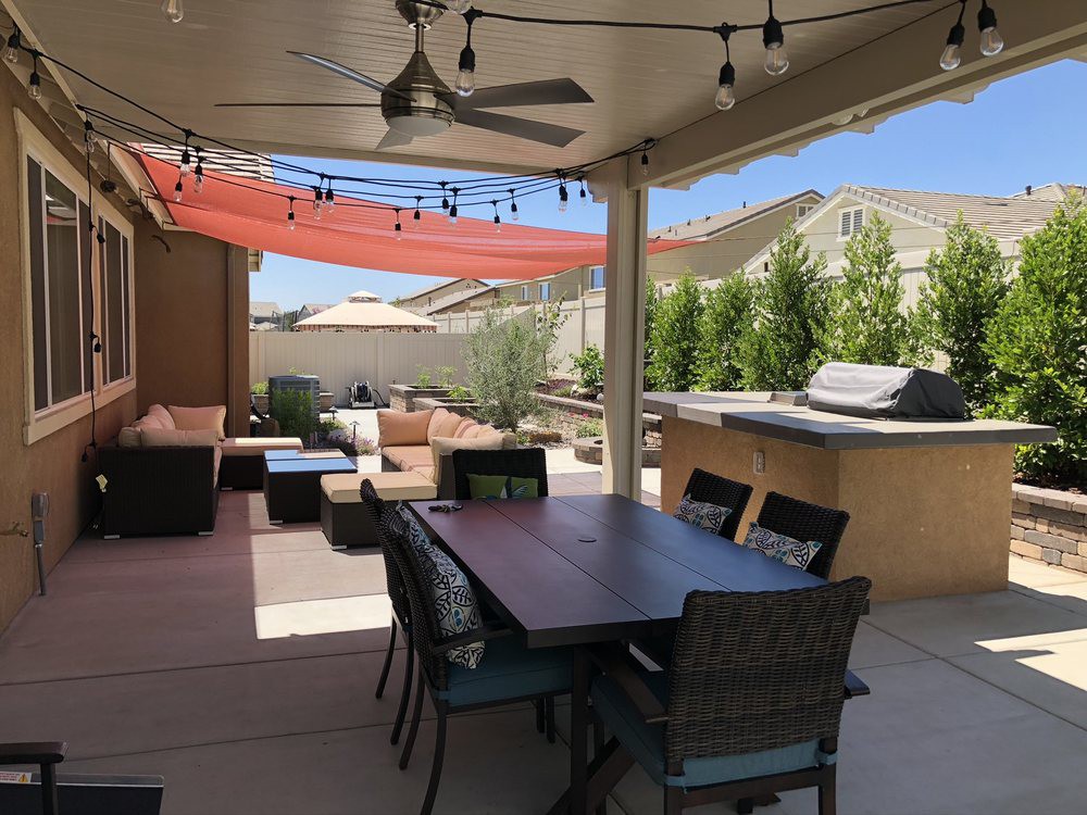 A cozy backyard patio with a dining area, lounge seating, and barbecue under string lights.