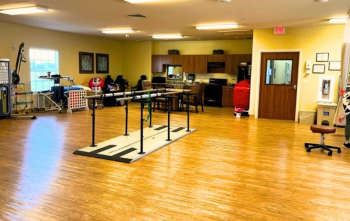 A therapy room featuring exercise equipment and a kitchen area, designed for rehabilitation activities.