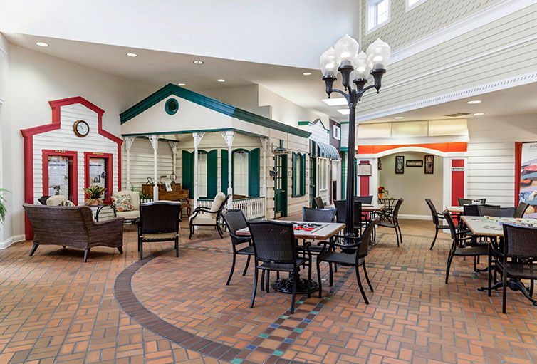 An indoor seating area featuring decorative house facades and street lamps, with tables and chairs on a brick floor.