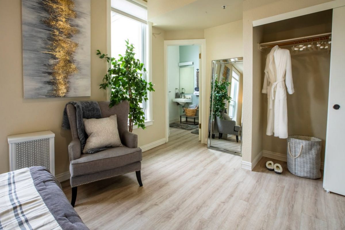 A modern interior space featuring an armchair, a standing mirror, and a glimpse into a bathroom.