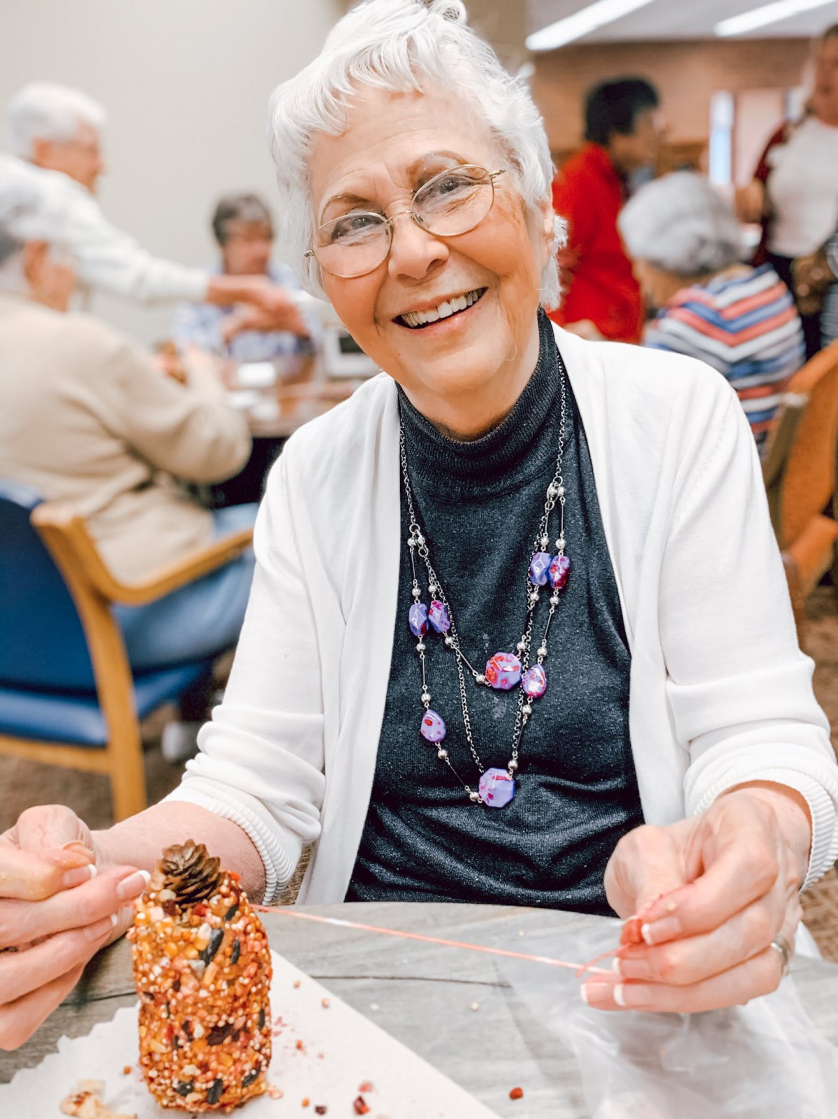 An elderly woman smiling while enjoying a meal at a social gathering.