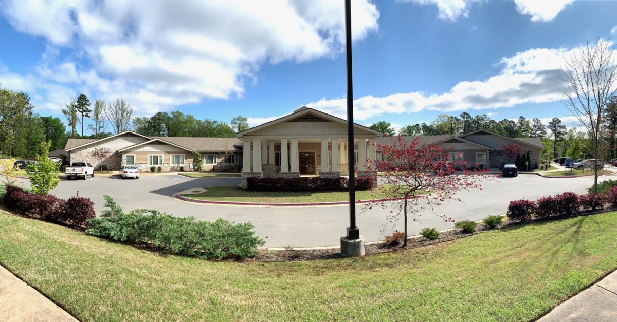 A scenic view of a building with a circular driveway, surrounded by greenery and under a partly cloudy sky.