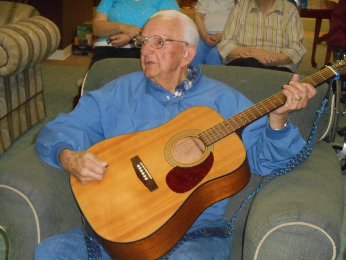 An elderly person playing a guitar indoors.