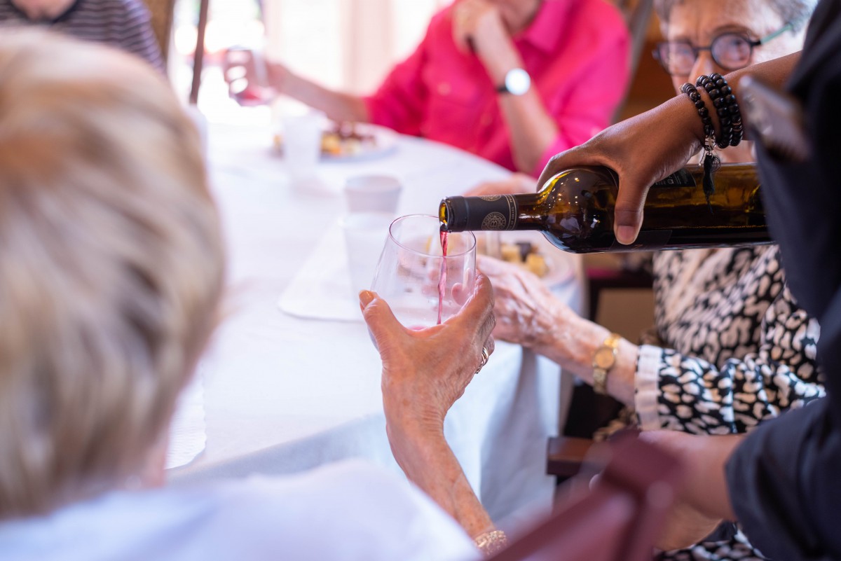 An elderly group enjoys a social gathering as wine is poured into glasses.