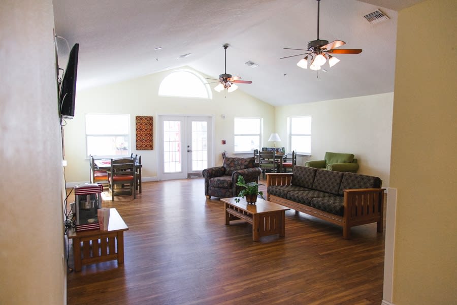 A spacious and bright living room with wooden floors, sofas, ceiling fans, and natural lighting.