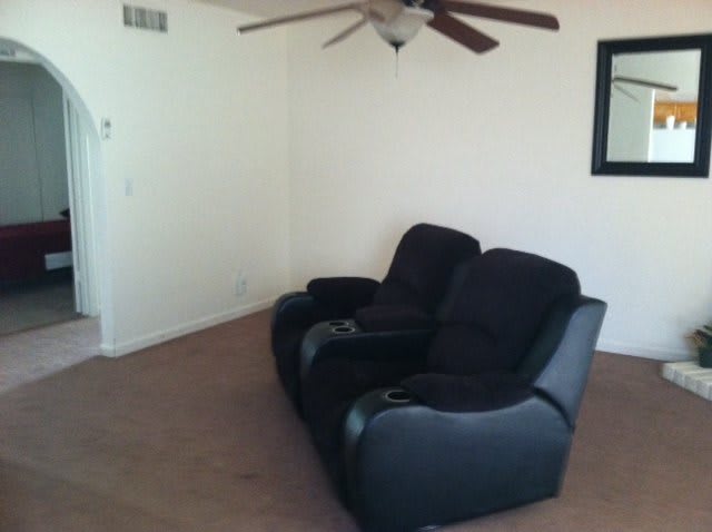 A minimalist living room with two black recliner chairs and a ceiling fan.