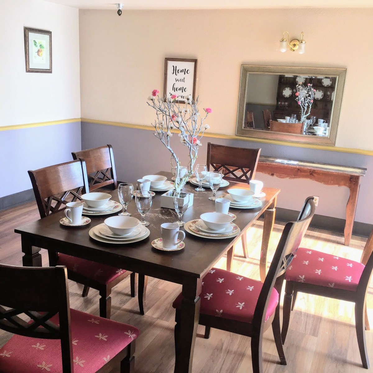 A dining room with a set table ready for a meal, featuring elegant dinnerware and red-cushioned chairs.