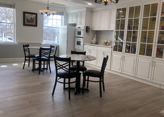 A modern kitchen and dining area with white cabinets, hardwood floors, and round tables with chairs.