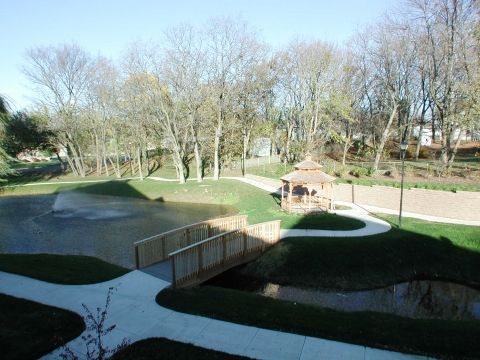 A sunny view of a park with a small bridge, winding pathways, and trees in the background.