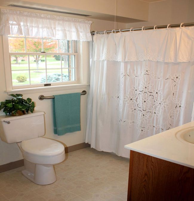 A bright and clean bathroom with a white shower curtain, toilet, indoor plant, and blue towel.
