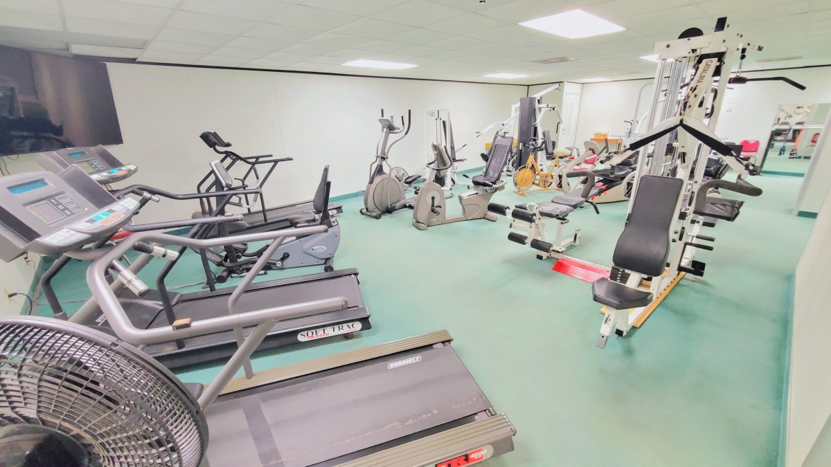 A gym room filled with various exercise equipment including treadmills, ellipticals, and stationary bikes.