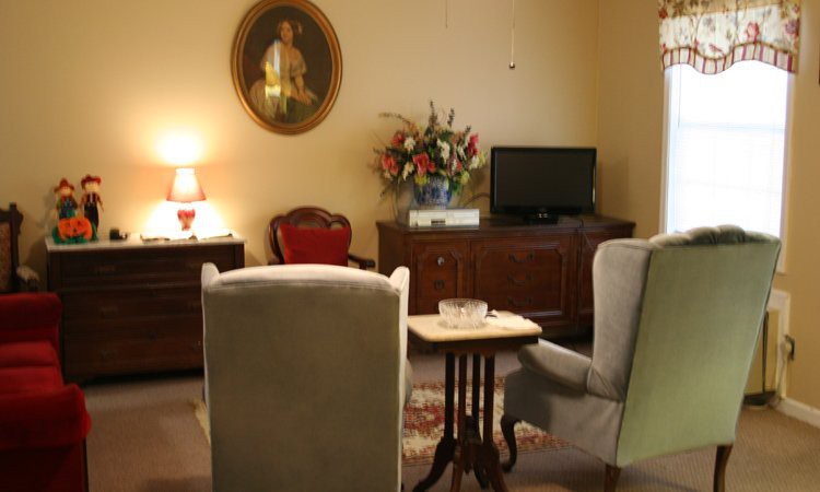 A cozy living room with traditional decor featuring armchairs, a television, and a portrait on the wall.