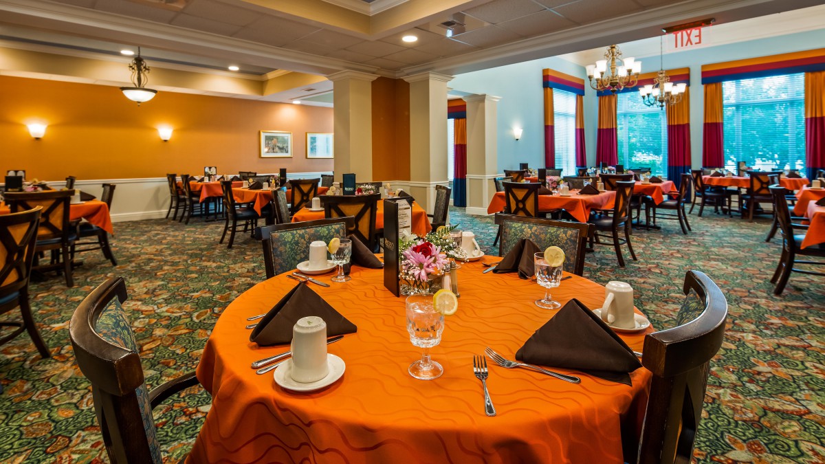 An elegantly set dining room with orange tablecloths and neatly arranged tables.