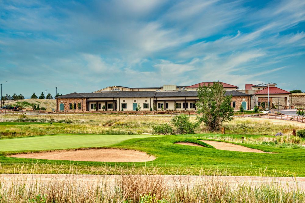 A scenic view of a golf course with a clubhouse in the background under a blue sky.