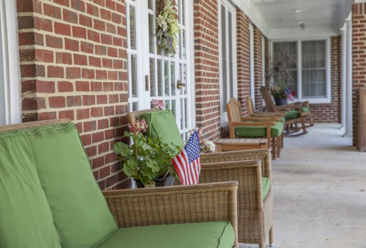 A cozy porch with wicker chairs and green cushions, adorned with plants and American flags.