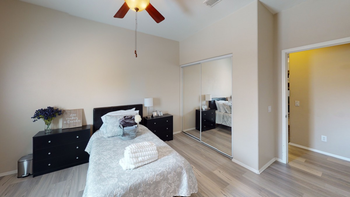 A cozy bedroom with a single bed, mirror closet, and ceiling fan.