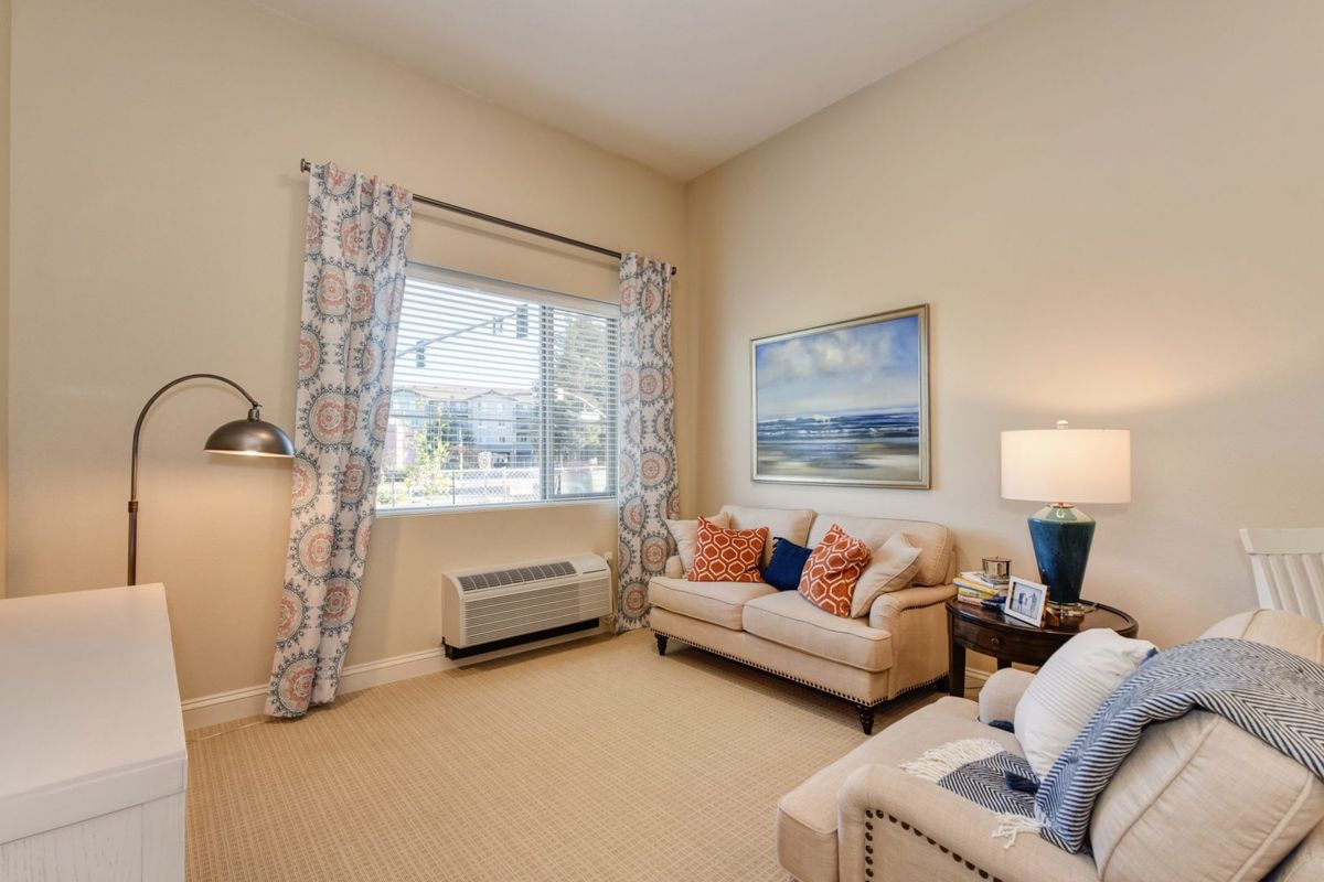 A cozy living room with a sofa, artwork on the wall, and a large window letting in natural light.