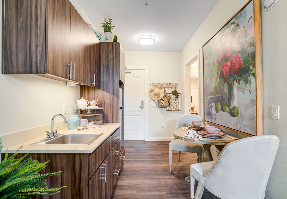 A modern kitchen with wooden cabinets and a cozy dining area, adorned with stylish decor and artwork.