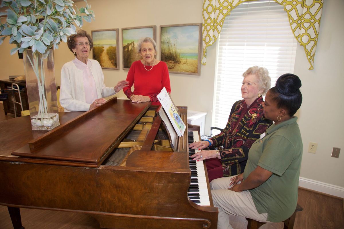 A group of people gathered around a piano singing together indoors.