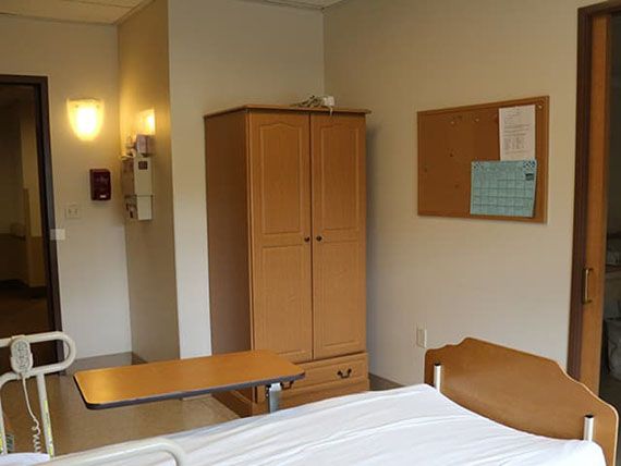 A hospital room with a wardrobe, bedside table, and notice board.