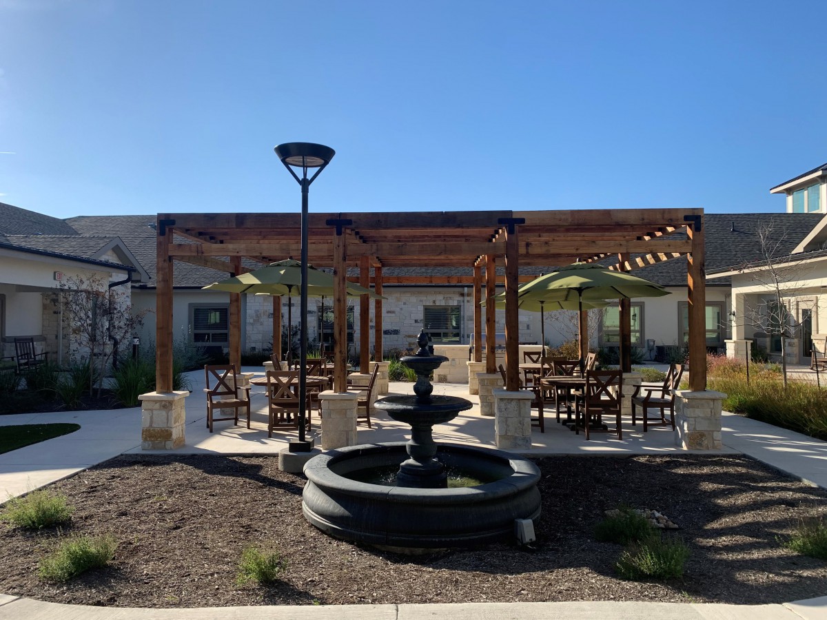 A sunny outdoor seating area with a pergola and a central fountain.