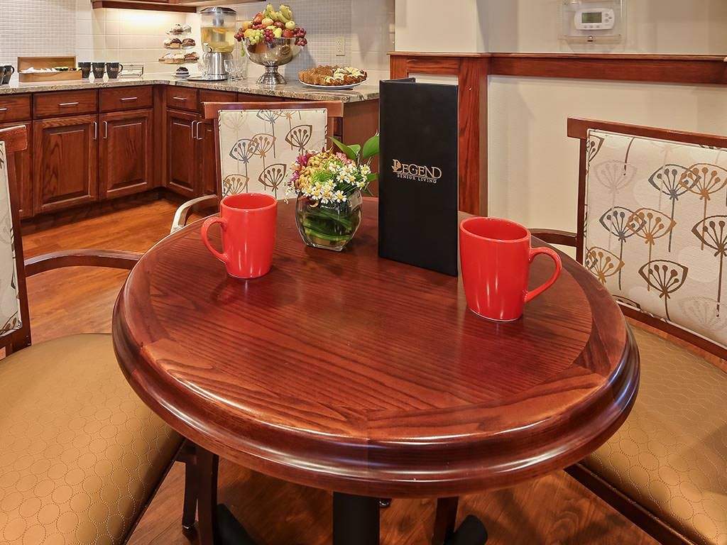 A cozy dining area with a round wooden table set for two, featuring red mugs and a menu.