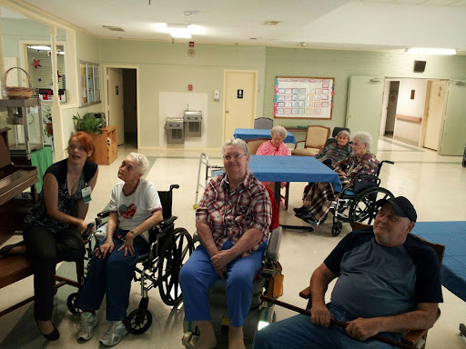 A group of elderly individuals seated in wheelchairs at a community center, engaged in conversation.